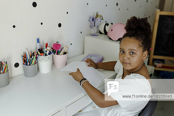 Smiling girl with paper sitting at desk at home