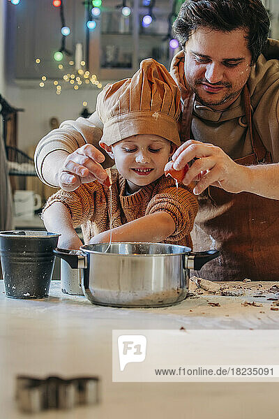 Smiling son with father cracking egg in utensil at home