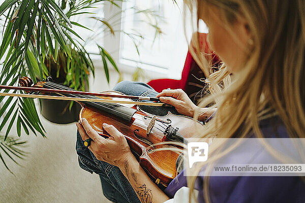 Violinist holding violin sitting in front of potted plant at studio