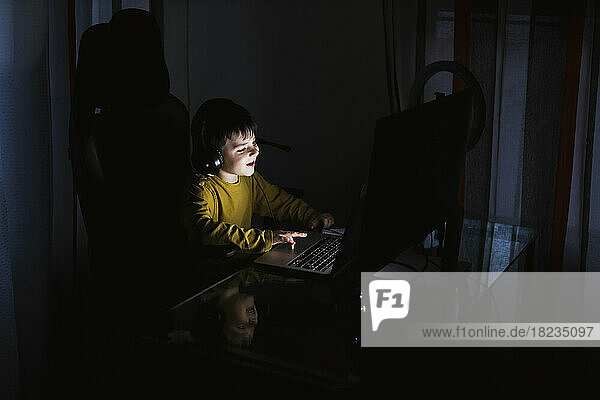 Boy wearing headphones using laptop on table at home