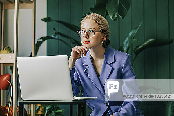 Nachdenkliche Geschäftsfrau mit Laptop sitzt im Heimbüro