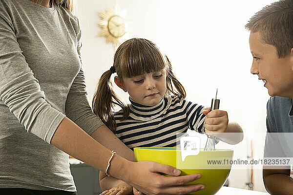 Boy looking at sister mixing ingredients in bowl by girl at home