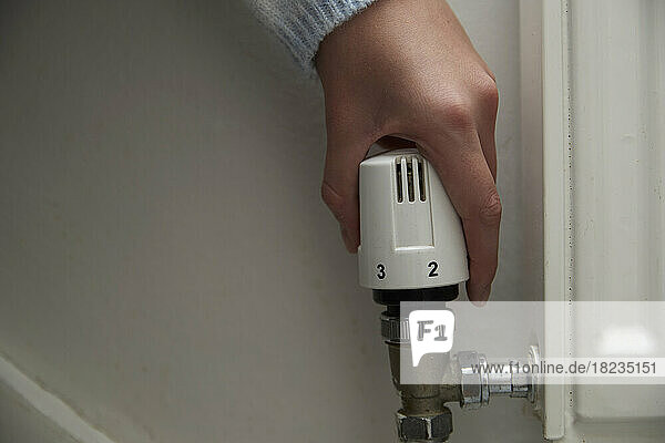 Hand of girl adjusting radiator thermostat regulator at home