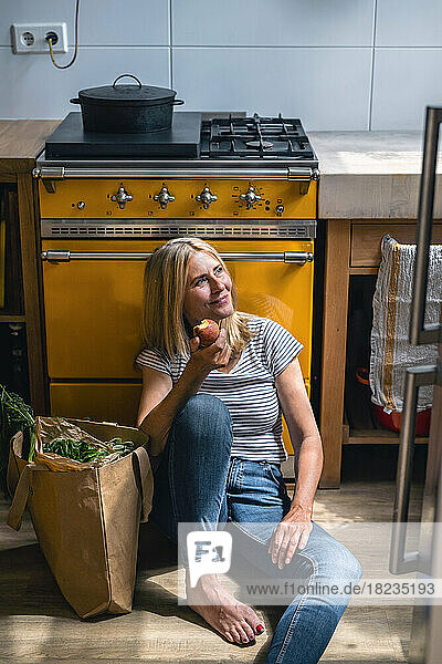Thoughtful woman sitting with apple in kitchen
