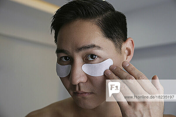 Young man applying eye mask at home