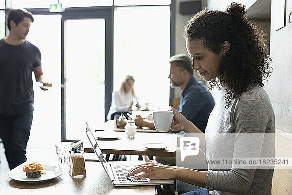 Smiling freelancer working on laptop drinking coffee at cafe