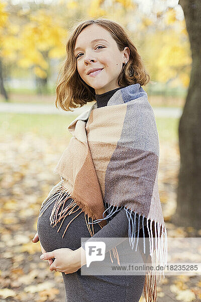 Smiling pregnant woman with shawl standing in autumn park
