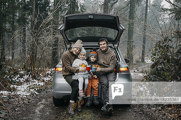 Happy family with coffee cups sitting in car trunk