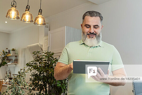 Smiling mature man using tablet PC with illuminated pendant lights in background at home