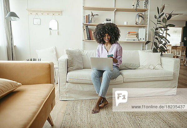 Smiling woman paying with credit card on laptop in living room