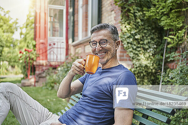 Happy man holding coffee cup on bench in garden
