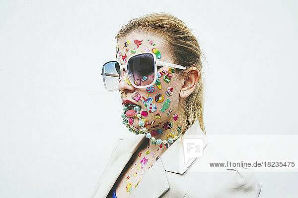 Woman with multi colored stickers on face and necklace in mouth against white background