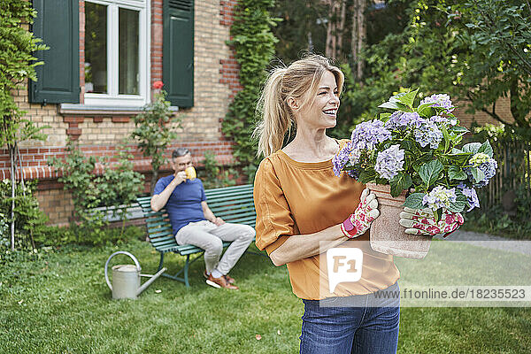 Happy woman looking at flowering plant with man in background