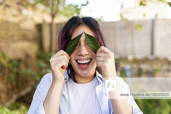 Happy woman holding leaves over eyes in garden