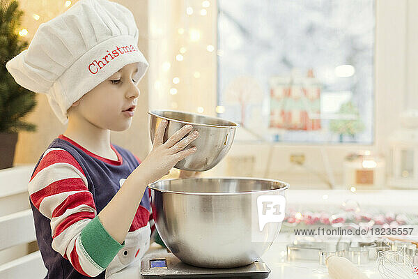 Boy wearing chef's hat preparing gingerbread cookies in kitchen