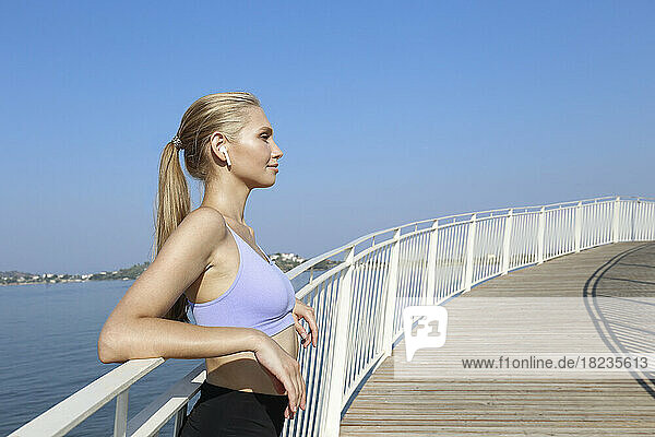 Young woman wearing wireless in-ear headphones leaning on railing
