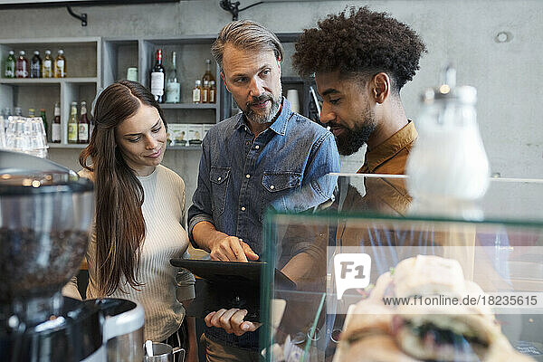 Coffee shop owner sharing tablet PC with baristas in cafe