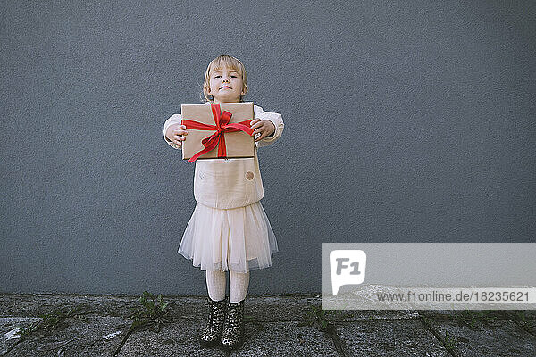 Girl holding gift box standing in front of concrete wall