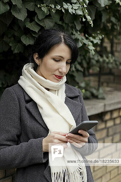 Woman wearing scarf using smart phone by plants