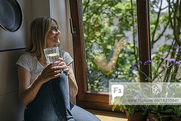 Mature woman day dreaming with glass of water near window