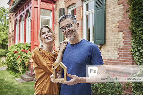 Happy woman standing by man holding house model in back yard