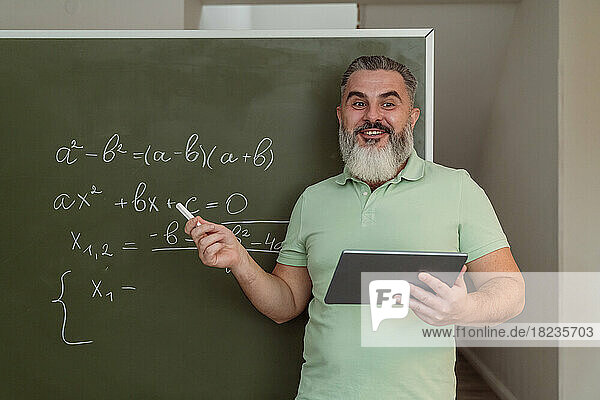 Reifer Lehrer mit Tablet-PC  der Mathematik an der Tafel unterrichtet