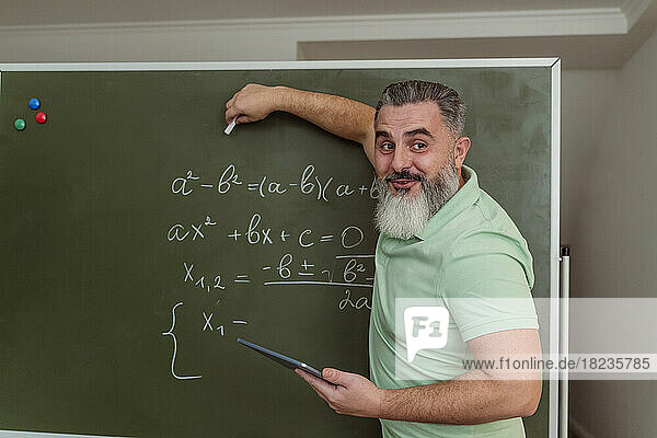 Teacher explaining mathematics on chalkboard holding tablet PC
