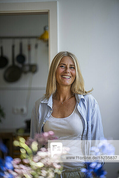 Happy mature woman with blond hair standing at home