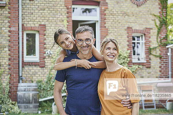 Smiling daughter with parents in front of house