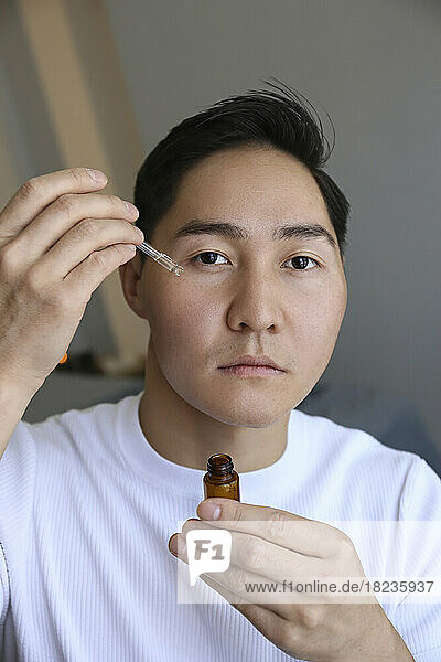 Young man applying CBD serum at home