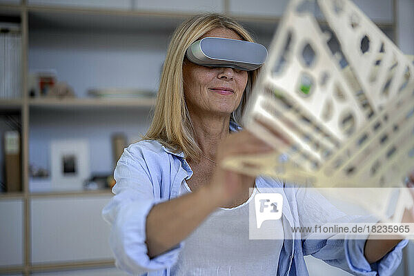 Smiling mature woman with VR glasses holding 3d print at home