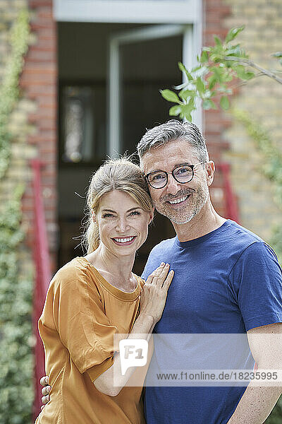 Smiling mature man embracing woman in front of house