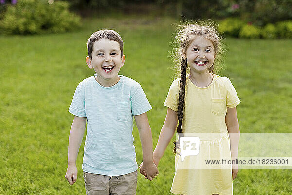 Fröhlicher Bruder und Schwester halten sich an den Händen und stehen im Garten