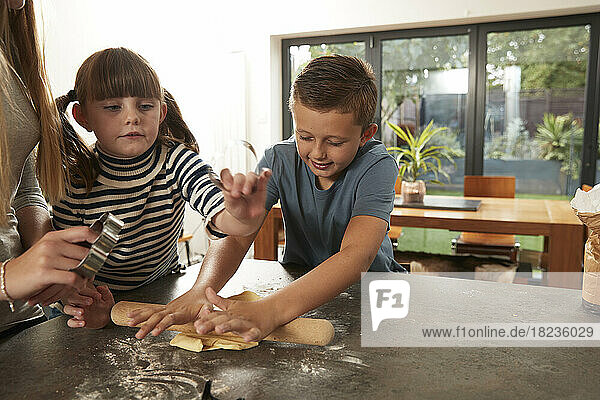 Smiling boy rolling dough by sisters at home