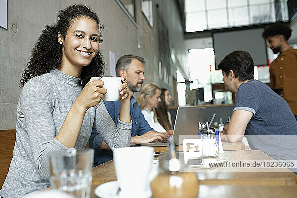 Smiling woman drinking coffee by customers in cafe