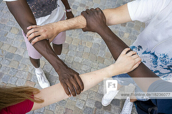 Multiracial friends holding hands together standing on footpath