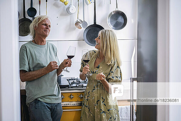 Happy mature woman with man holding glass of red wine in kitchen