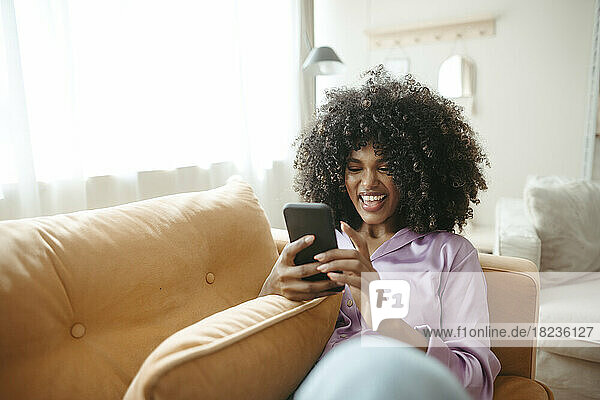 Happy woman using mobile phone sitting on sofa