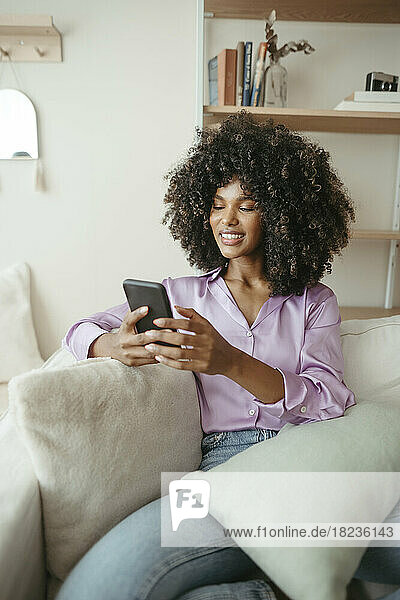 Smiling woman using smart phone sitting on sofa at home