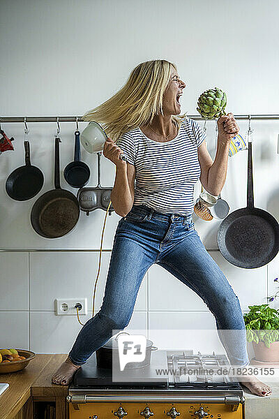 Carefree woman having fun enjoying with artichoke in kitchen