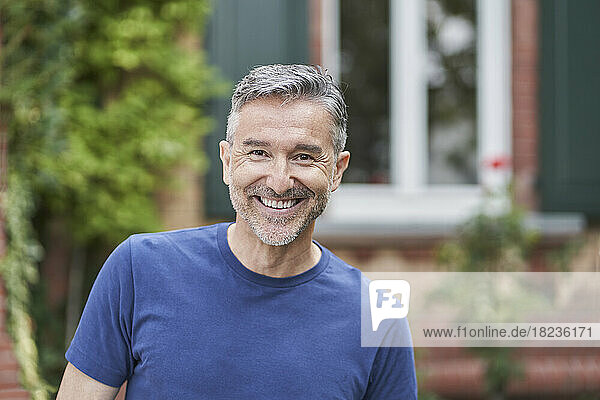 Happy man with gray hair in front of house