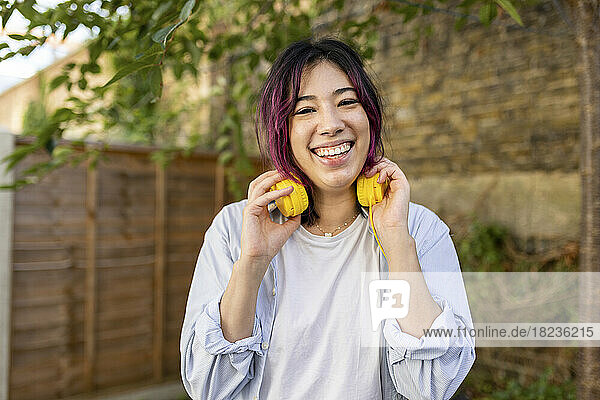 Happy young woman with headphones standing in garden