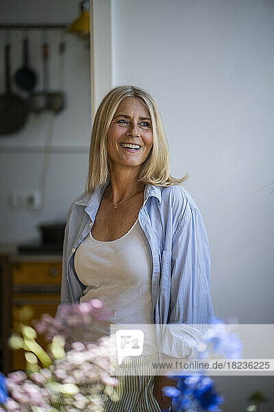 Smiling mature woman with blond hair standing at home