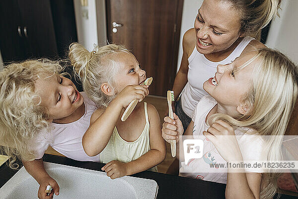 Mutter beobachtet Töchter beim Zähneputzen mit Holzbürsten in der Küche