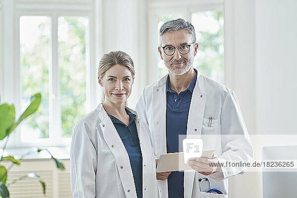 Smiling female doctor with colleague holding tablet PC at medical practice
