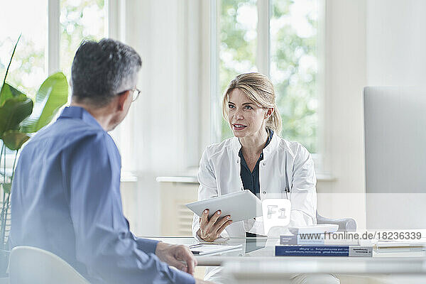Female doctor giving advice and discussing with patient over tablet PC at medical practice