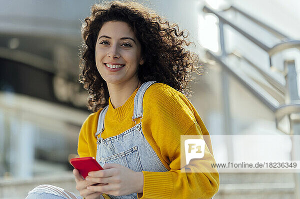 Smiling woman with curly hair holding mobile phone