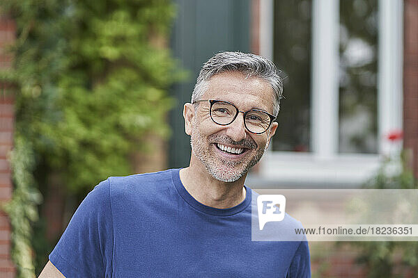Happy man wearing eyeglasses in front of house