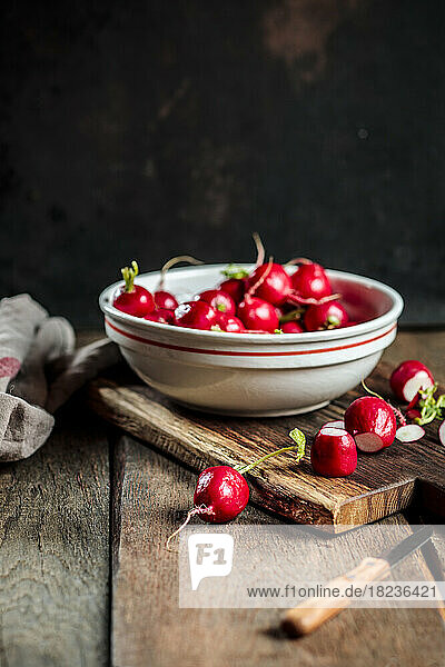 Fresh radishes in bowl with knife on table