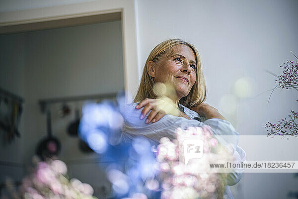 Thoughtful mature woman hugging herself at home
